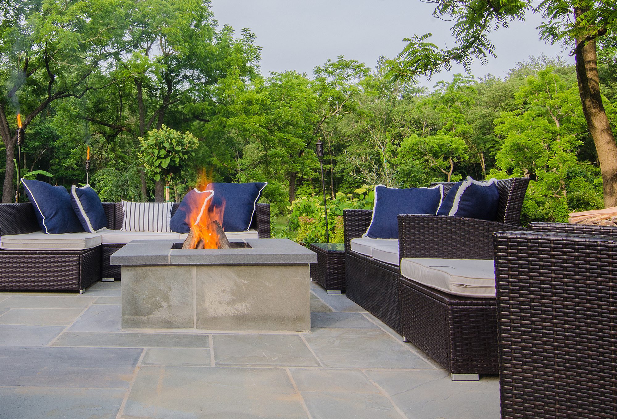 A wood-burning fire burns in a fire pit surrounded by chairs and pillows.