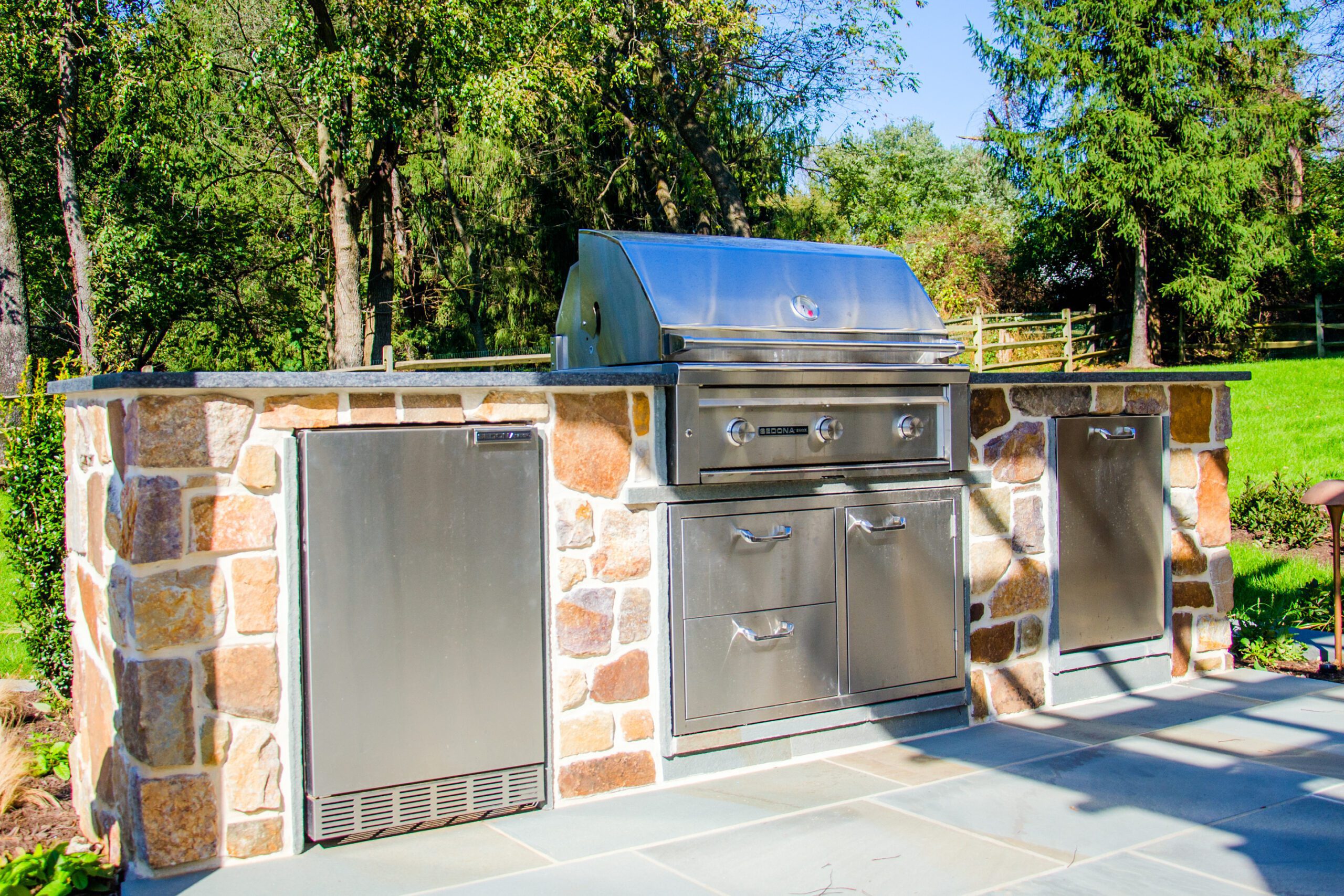 An outdoor kitchen features a refrigerator, grill, and sink.