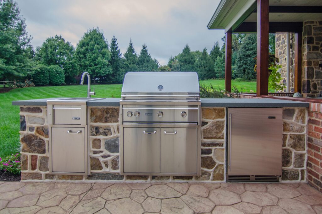 An outdoor kitchen features a sink, built-in grill, and refrigerator.