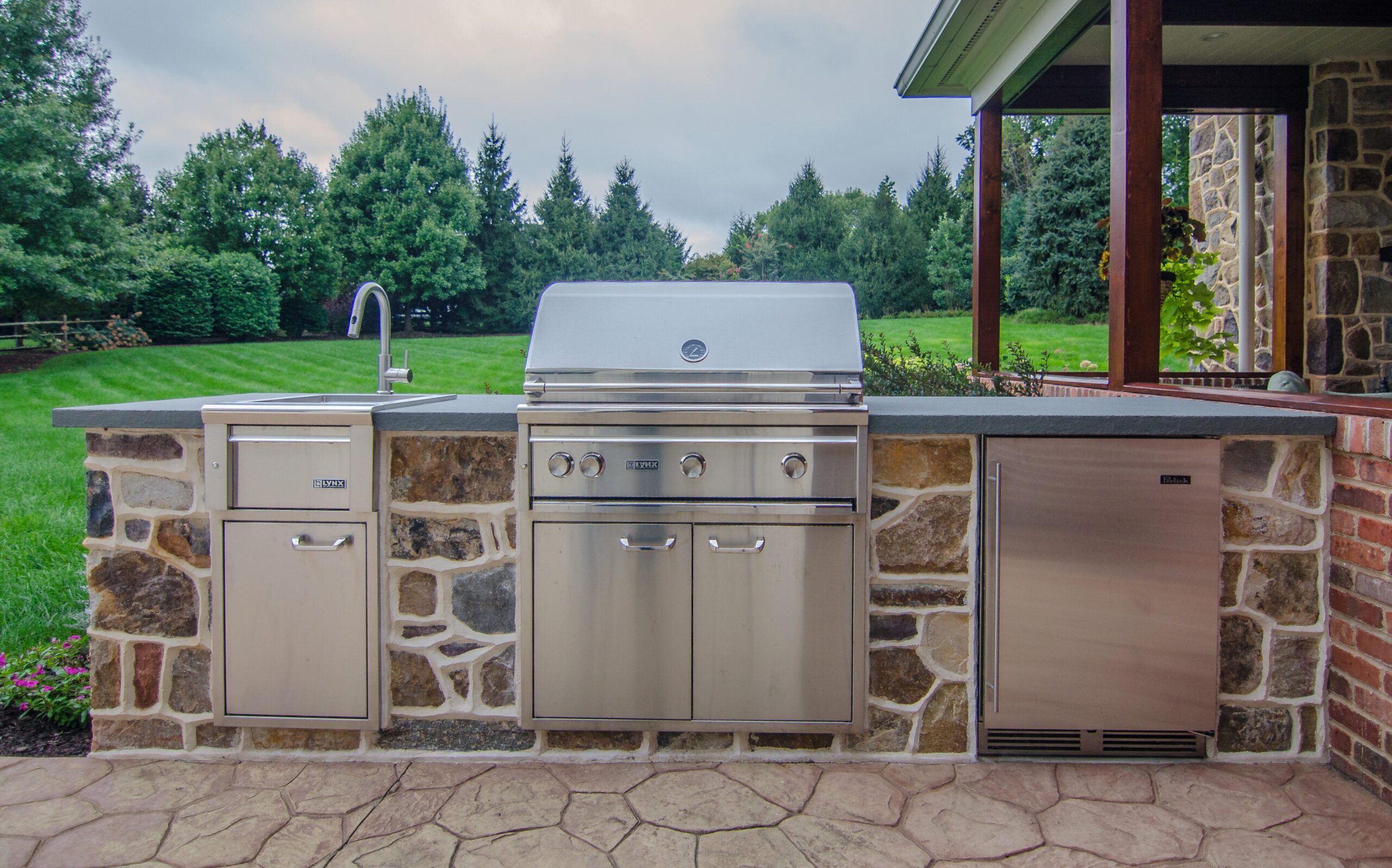 An outdoor kitchen features a sink, built-in grill, and refrigerator.