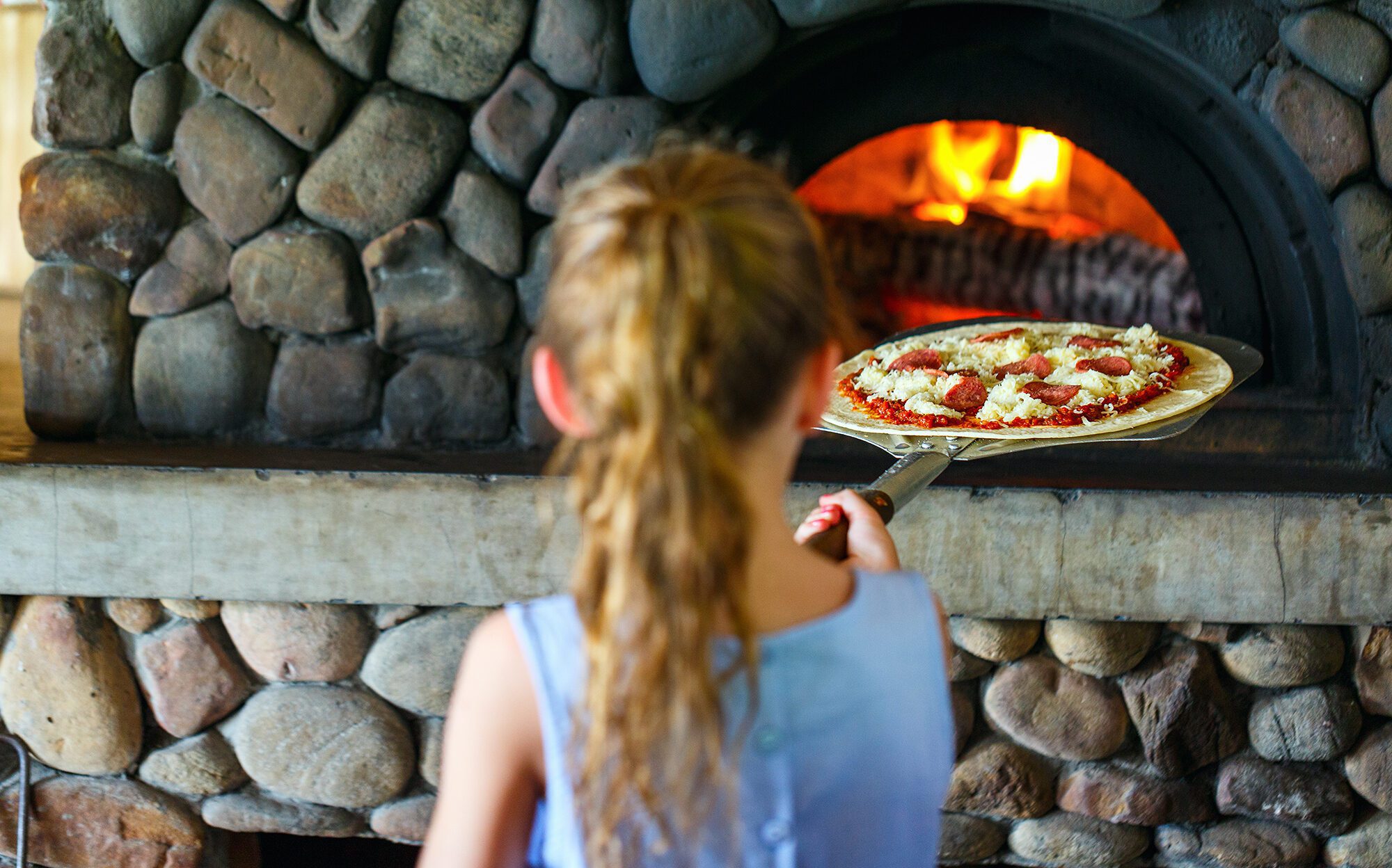 Young girl putting pizza into an outdoor pizza oven