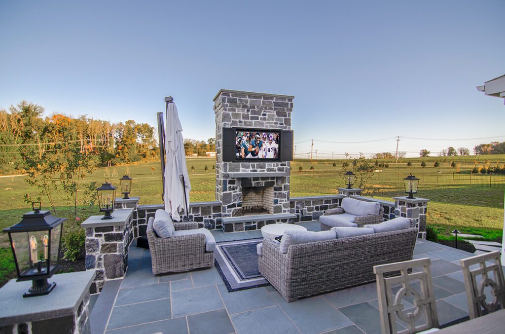A backyard fireplace with a TV on the chimney surrounded by furniture.