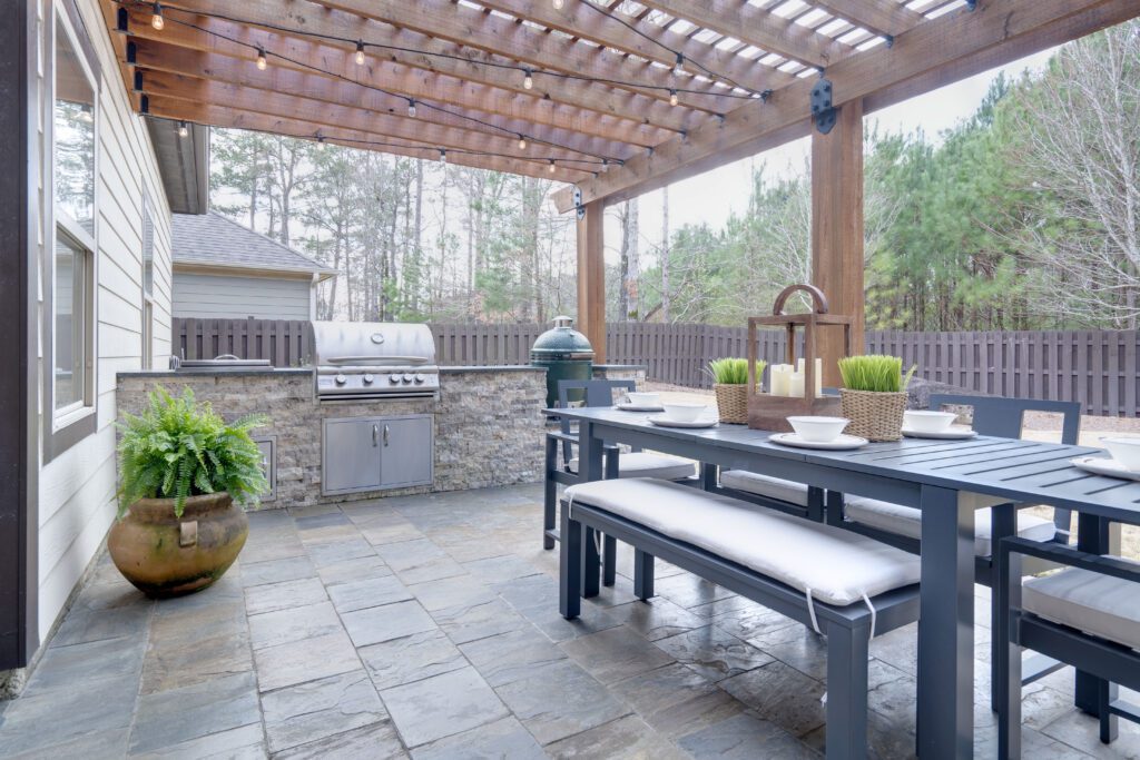 An outdoor kitchen on a stone patio with a table and grill.